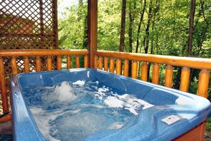A hot tub on an outdoor deck with wooden railings and a forested background. - Downtown Cabin|Private Pool|Hot Tub|Game Room (PIGEON FORGE)