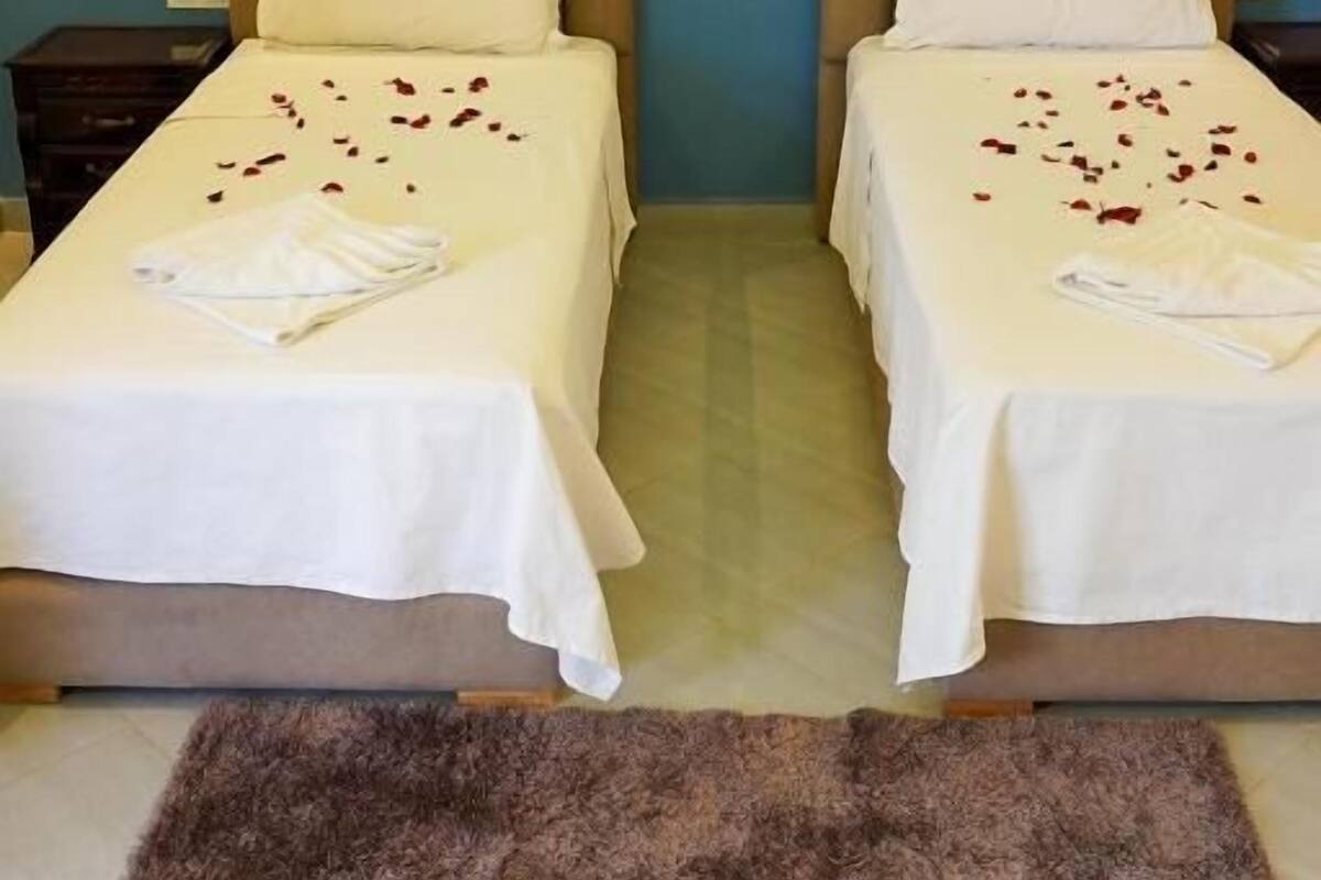 Two single beds with headboards, white linens, and scattered rose petals.