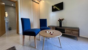 A modern living room with two blue chairs, a round coffee table, and a flat-screen TV mounted on the wall. - Dar Fatima Tamazouzt (Tamazouzte)