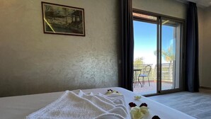 A hotel room with a large bed, a painting on the wall, and a balcony with a view. - Dar Fatima Tamazouzt (Tamazouzte)