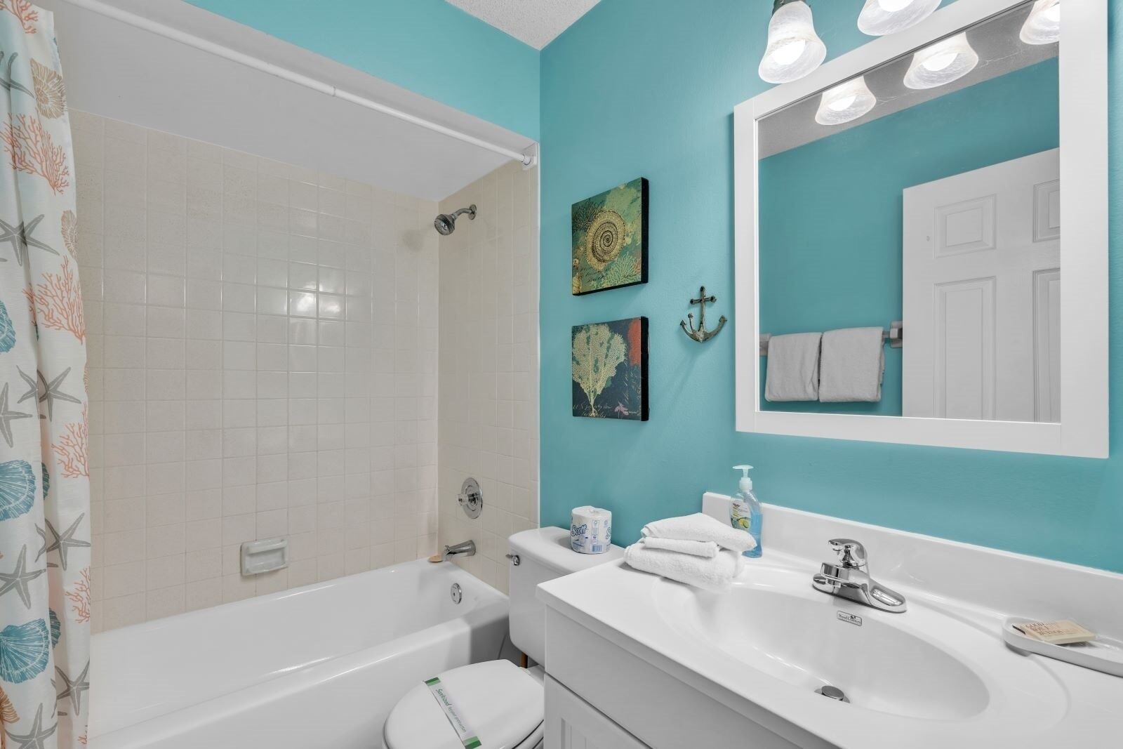Ein Badezimmer mit einer Badewanne, einem Waschbecken und einer Toilette. An der Wand hängen zwei gerahmte Kunstwerke, ein Handtuchhalter und ein Spiegel über dem Waschbecken.