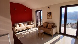 Un soggiorno moderno con una parete di accento rosso, due divani, un tavolino da caffè e ampie finestre con vista sul mare.