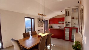 Una cucina moderna con mobili rossi, un'area pranzo con tavolo e sedie in legno, e vista all'esterno attraverso un'ampia finestra.