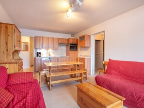 Un espacio habitable compacto con kitchenette, comedor y sofá rojo.