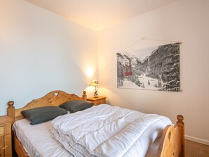 Un dormitorio con una cama de madera, una mesita de noche, una lámpara y un cuadro colgado en la pared con una vista nevada de la montaña.