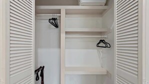 A white closet with sliding doors, featuring multiple shelves and hanging space.