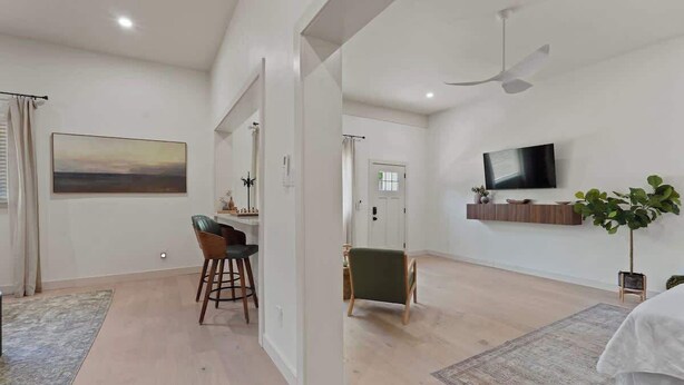 A spacious living area with a flat-screen TV mounted on the wall, a ceiling fan, and a small plant on a stand.