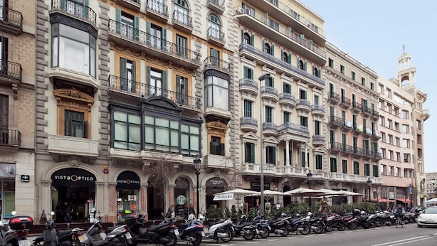 Une rangée de bâtiments historiques dotés de nombreux balcons, de boutiques, dont un Starbucks, et une rangée de scooters garés.