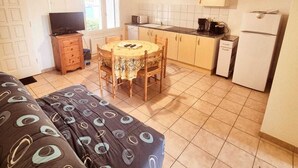 Ein kompakter Wohnraum mit Sofa, Esstisch und Stühlen, einer Küchenzeile inklusive Schränken und Geräten sowie einem Fernseher.