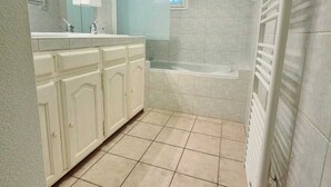 Ein Badezimmer mit einer Badewanne, einer Dusche, einem Waschbecken inklusive Spiegel und einem Handtuchhalter.