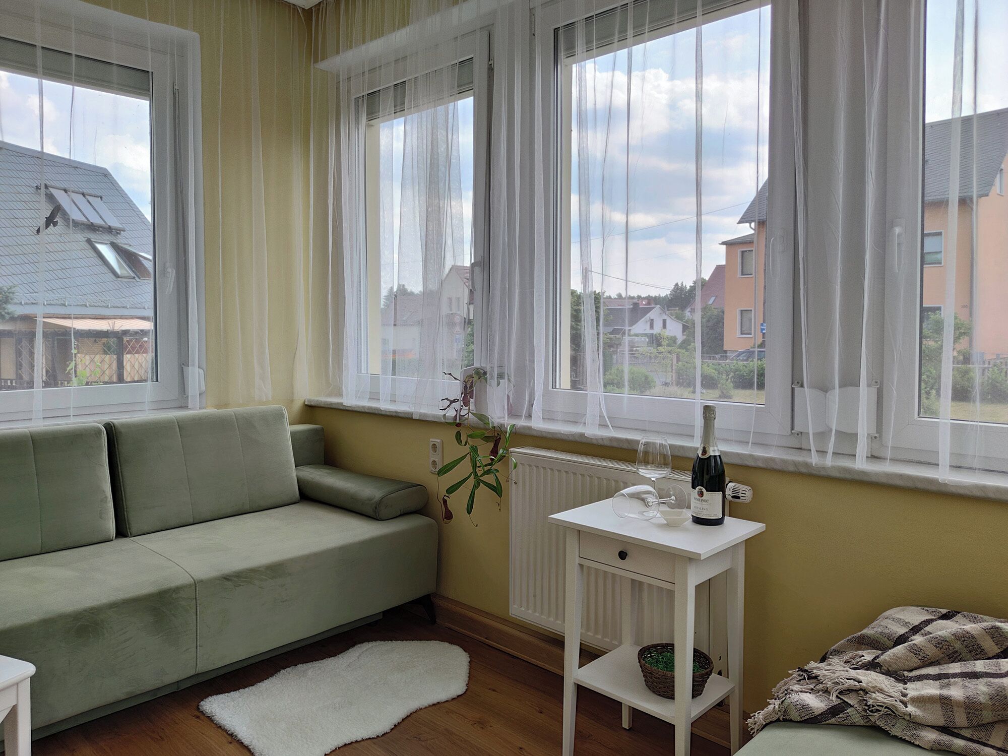 Ein Zimmer mit einem grünen Sofa, einem weißen Heizkörper und einem Tisch mit Flasche und Glas.