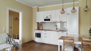 Une cuisine moderne avec des meubles blancs, une table à manger en bois et des luminaires suspendus.