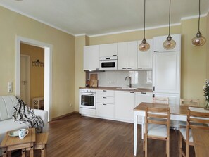 A modern kitchen with white cabinets, a wooden dining table, and hanging pendant lights. - Rock magic: Romantic apartment in Gohrisch (Gohrisch)