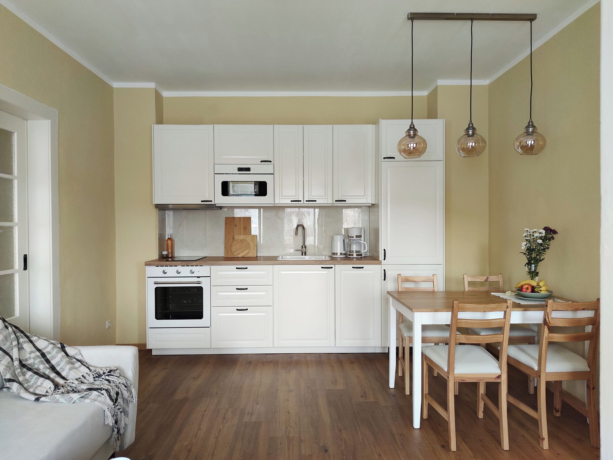 Eine kleine Küche mit weißen Schränken, einer Mikrowelle, einem Backofen und einem Essbereich mit Holztischen und einem Tisch.