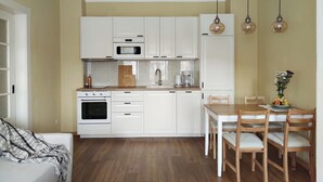 Une cuisine compacte avec des meubles blancs, un four à micro-ondes, un four traditionnel et un coin repas comprenant des chaises et une table en bois.