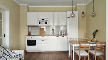 Eine kleine Küche mit weißen Schränken, einer Mikrowelle, einem Backofen und einem Essbereich mit Holztischen und einem Tisch.