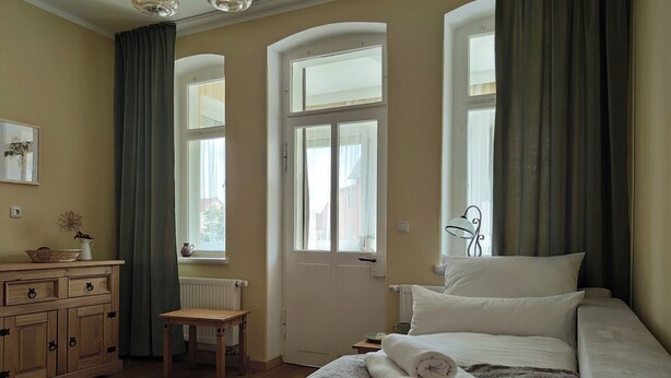 Une chambre à coucher avec un lit, une commode, une chaise et une fenêtre avec des rideaux.