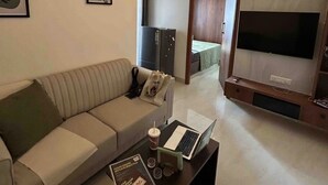 Uma sala de estar moderna com um sofá, uma mesa de centro com um laptop e uma bebida, uma TV e um ventilador de teto.