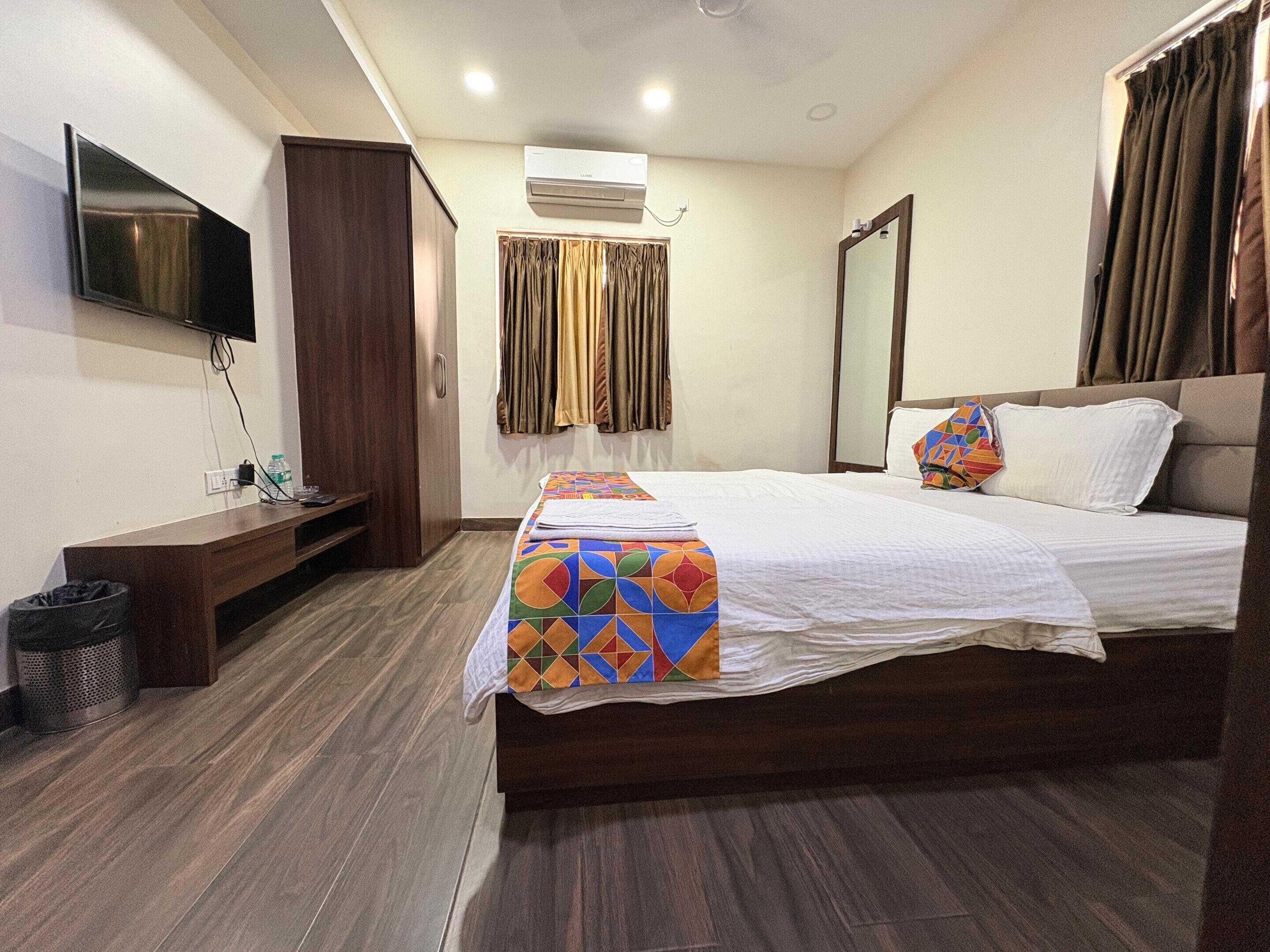 Una habitación de hotel con una cama, un televisor en la pared, un escritorio y un cubo de basura.