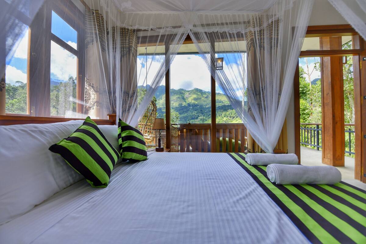 Un dormitorio con una cama grande, un balcón con baranda de madera y vistas a vegetación exuberante.