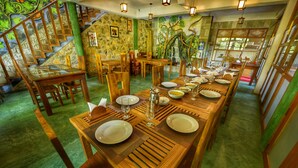 A dining area with a long wooden table set for a meal, surrounded by wooden chairs.