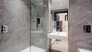 Et moderne badeværelse med en glasafskærmet brusekabine, et hvidt håndvaskarrangement og et stort spejl.