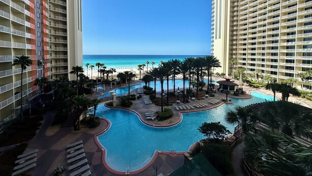 A resort with a pool, palm trees, and a beach view. - Beachfront Condo w/ Free round of Golf & Activities Daily! (Panama City Beach)