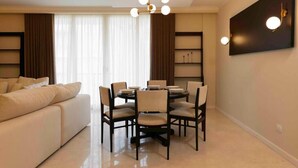 Een moderne woonkamer met een ronde eettafel, beige banken en een kroonluchter.