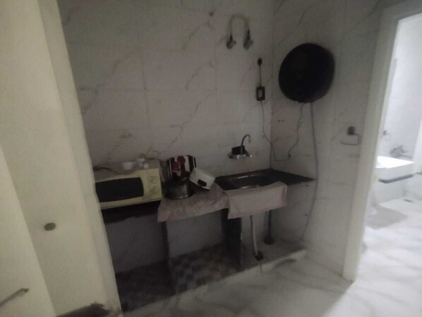 A small, compact kitchen with a sink, a microwave, and a hanging pot rack. - East Delhi Stays Inn (New Delhi)
