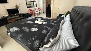 A hotel room with a bed, a desk, a TV, and a dining area with chairs. - One Palm Tree Villas Across MNL Airport T3 (Pasay)