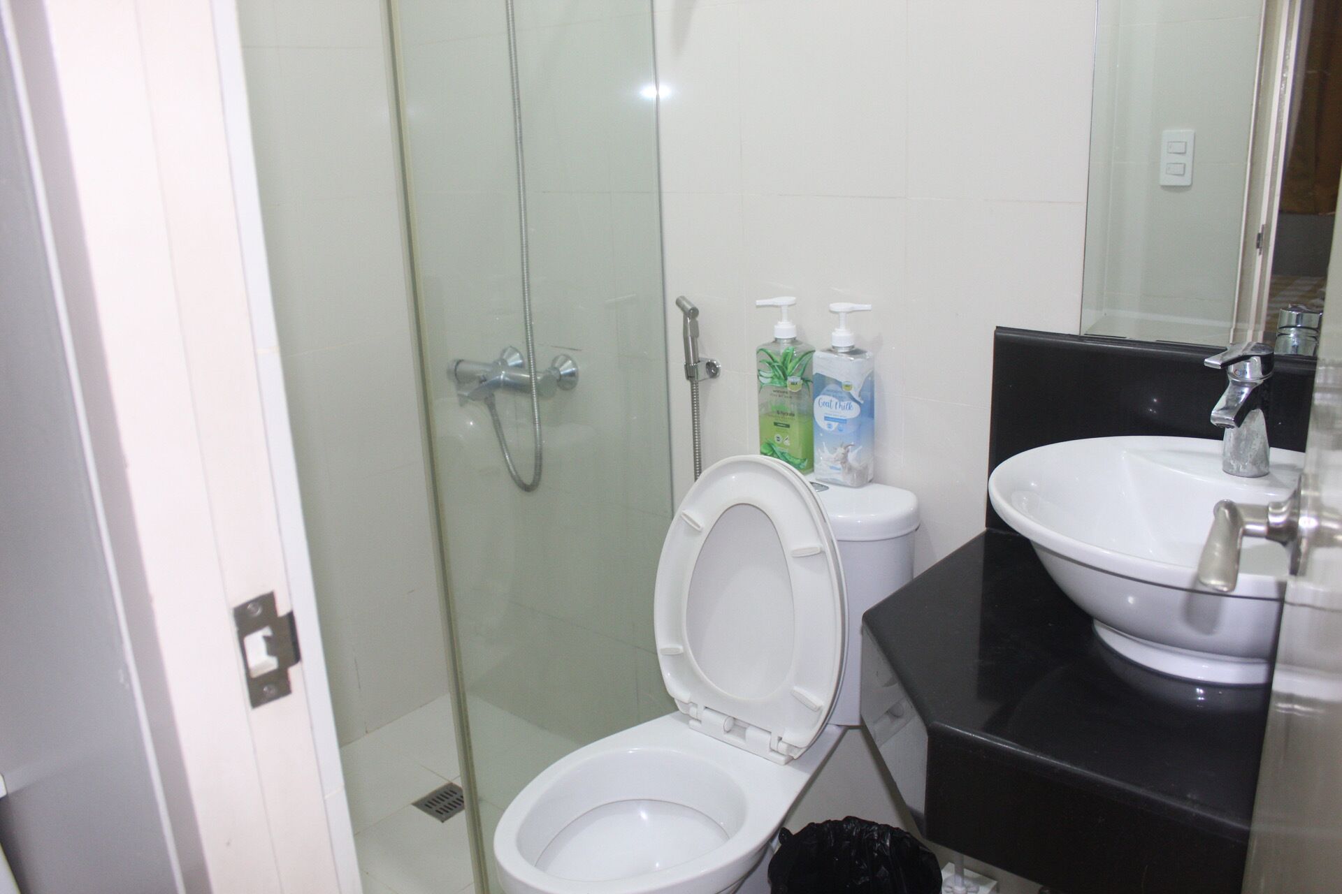 A bathroom with a glass-enclosed shower, a white toilet, and a black sink.