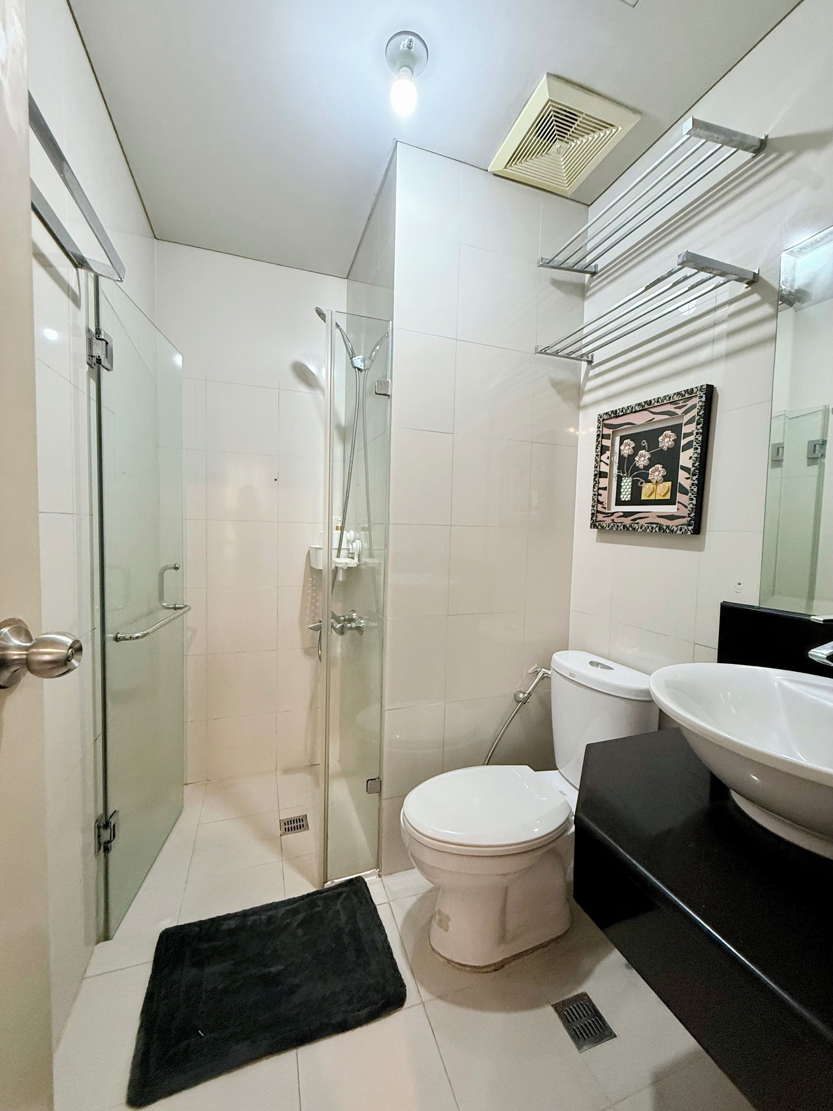 A bathroom with a glass-enclosed shower, a white toilet, a black mat, and a sink with a black countertop.