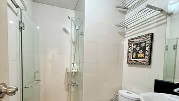 A bathroom with a glass-enclosed shower, a white toilet, a black mat, and a sink with a black countertop.