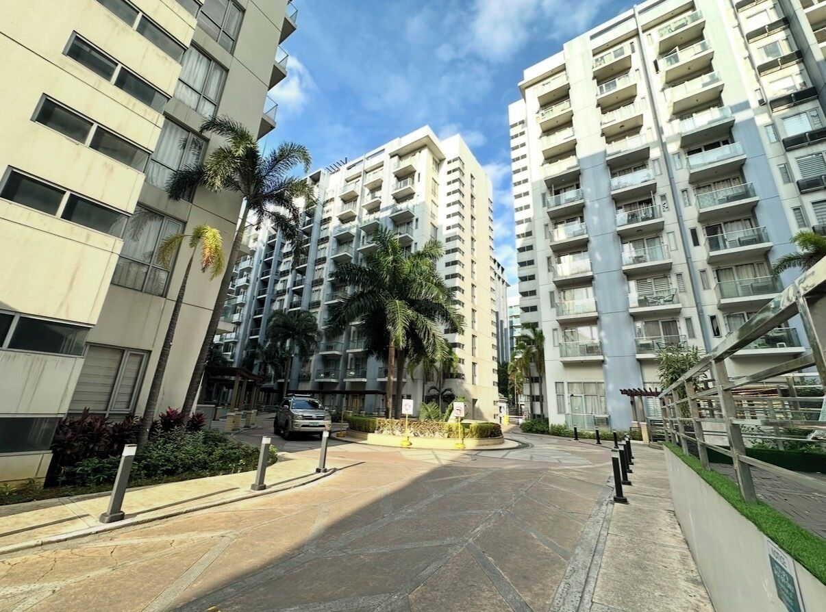 A residential area with high-rise buildings, a paved road, and a small roundabout with palm trees.