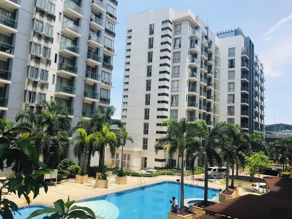 A modern residential building with multiple balconies, a swimming pool, and surrounding greenery. - One Palm Tree Villas Across MNL Airport T3 (Pasay)