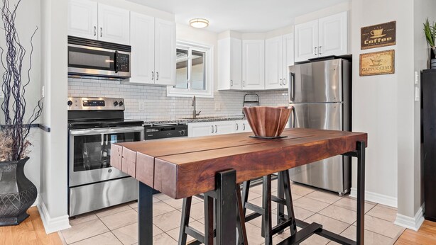 A modern kitchen with white cabinets, stainless steel appliances, and a wooden bar stool. - Cozy, Quiet Home in Kingston. Short drive to Queen's University. Pet Friendly! (Kingston)