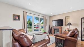 A modern living room with leather sofas, a flat-screen TV, and large windows offering a view of the outdoors. - Cozy, Quiet Home in Kingston. Short drive to Queen's University. Pet Friendly! (Kingston)