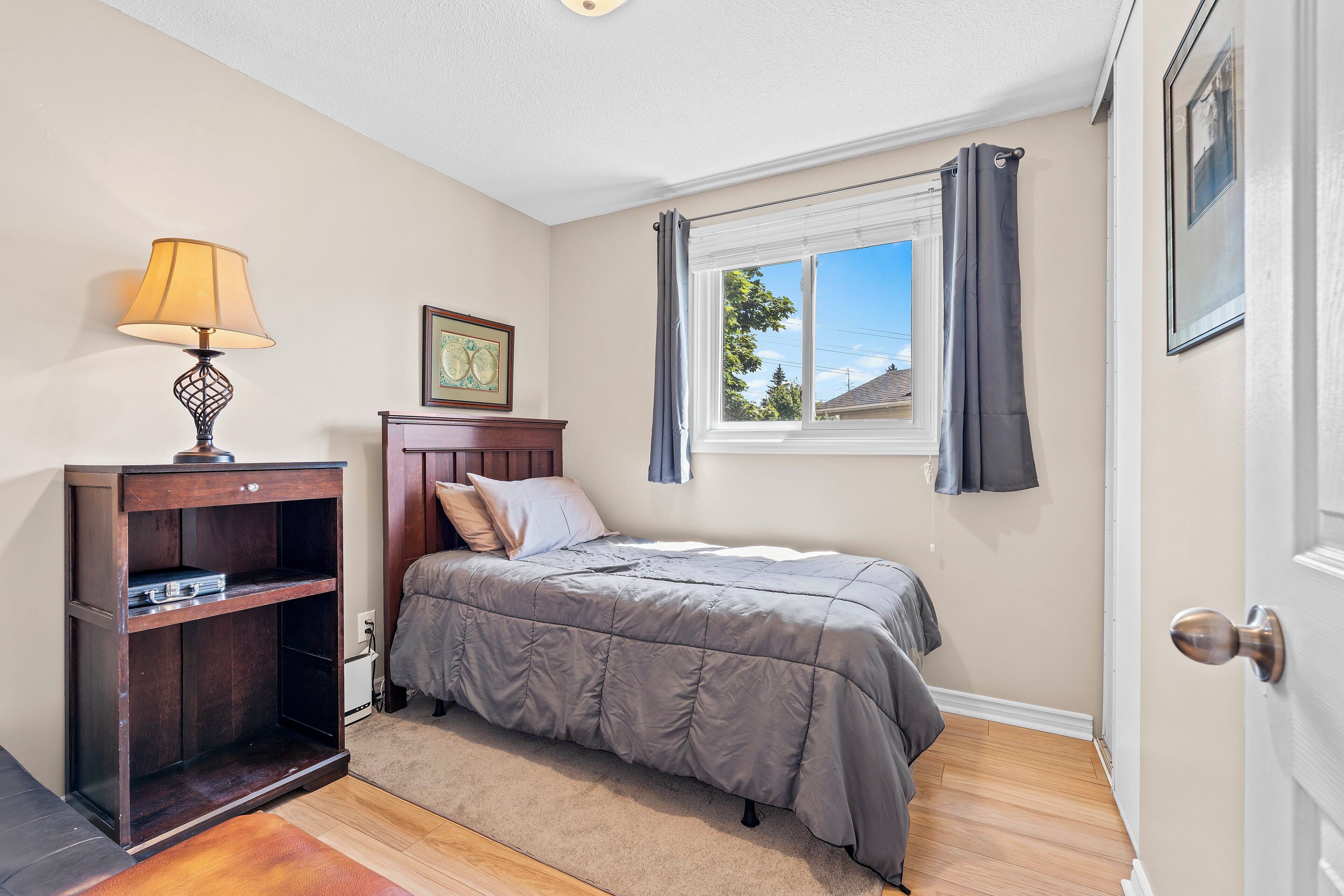 A bedroom with a bed, a nightstand, a lamp, a window with curtains, and a door.