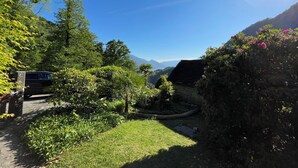 Un jardí exuberant amb un camí de pedra, una construcció de fusta i una muntanya al fons.