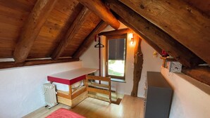 Un petit i acollidor dormitori a l'àtic, amb sostre inclinat, un llit individual, un escriptori i una finestra amb persianes.