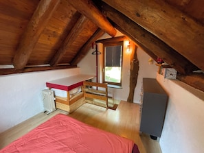Ett litet, ombonat rum på vinden med ett sluttande tak, en enkelsäng, ett skrivbord och ett fönster med persienner.