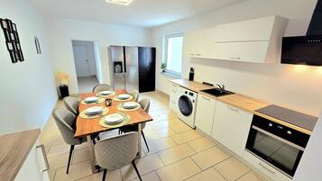 A modern kitchen with a dining area, a washing machine, and a built-in oven.