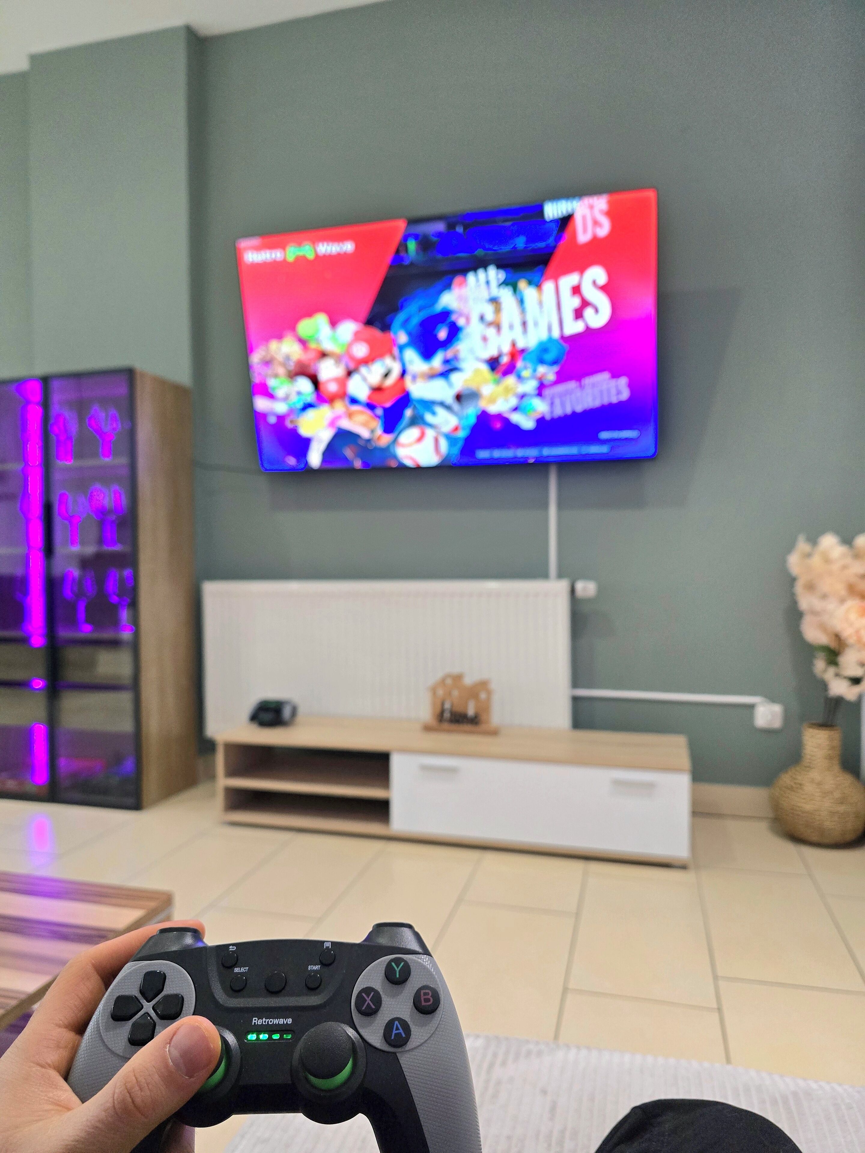 A living room with a television displaying a video game, a gaming console, and a decorative vase.