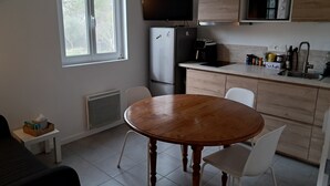 A compact kitchen with a dining table, chairs, a refrigerator, a coffee maker, and a TV mounted above the counter. - SAINT-JEANNET, Village in the Préalpes d'Azur, near NICE, SAINT-PAUL-DE-VENCE (Saint-Jeannet)