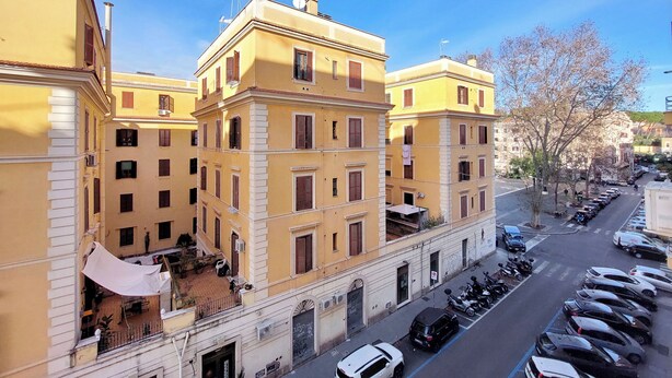 A multi-story yellow building with a courtyard, parked cars, and a clear sky. - Casa Lenilli - Beautiful apartment in Testaccio (Roma)