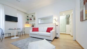 A modern living room with a white sofa, red cushions, a glass coffee table, and a grey rug. - Casa Lenilli - Beautiful apartment in Testaccio (Roma)