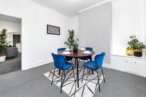 A dining area with a round table, blue chairs, and a patterned wall. - Chorlton House | Free Parking | 2BR Stoke-on-Trent (Stoke-on-Trent)