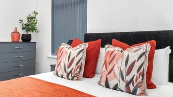 A bedroom with a bed, a nightstand, a dresser, and a window with blinds.