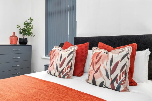 A bedroom with a bed, a nightstand, a dresser, and a window with blinds.