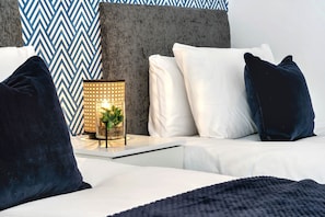 A modern bedroom with a sofa, pillows, a bedside table with a lamp, and a patterned wall.